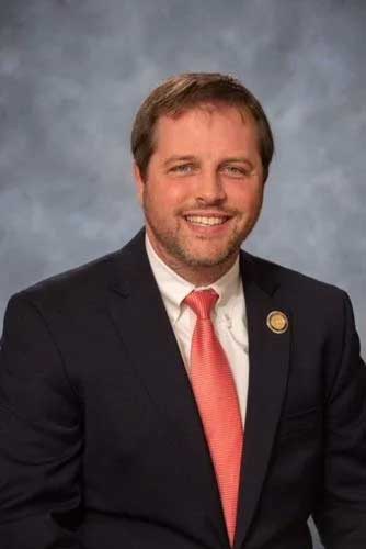 Representative Atkinson is smiling and wearing a round lapel pin bearing the seal of the state legislature.